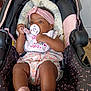 baby, infant, pacifier, headband, stroller, pink_socks, floral_outfit, child, cute, indoors, seat, comfort, portrait, young_child, clothing, baby_accessory, relaxing, small_person, adorable, baby_bib