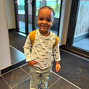 Mokeli participe au concours pour gagner de l'argent avec cette photo : child, smiling, indoor, backpack, white_shirt, crocodile_pattern, pants, sneakers, tile_floor, glass_door, natural_light, portrait, standing, young_child, happy, casual_clothing, boy, short_hair, modern_interior, daylight