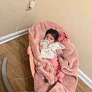 Amaia is registered to the contest to win money with this photo: baby, bottle, blanket, baby_rocker, child, curly_hair, floor, feeding, furniture, indoor, milk, person, plush, pink, portrait, resting, sitting, soft, toy, wood_floor