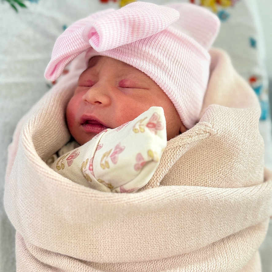 Annelise is registered to the contest to win money with this photo: newborn, baby, infant, sleeping, pink_hat, swaddled, blanket, floral_bedding, portrait, face, closed_eyes, peaceful, cozy, indoors, textile, soft_lighting, headwear, infant_clothing, nursery, photography