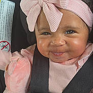 Ava is registered to the contest to win money with this photo: baby, car_seat, child, closeup, curly_hair, cute, face, happy, headband, indoor, infant, person, pink_bow, pink_clothing, plush_toy, portrait, safety_belt, seatbelt, smile, soft_toy