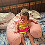 baby, bed, blanket, child, comfort, curly_hair, cute, diaper, indoor, infant, pacifier, patterned_fabric, person, pink_pillow, relaxed, skin, sleeping_area, soft_furnishing, wooden_headboard, yellow_dress