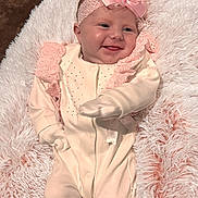 Navi is registered to the contest to win money with this photo: baby, infant, smile, headband, bow, blanket, soft_texture, pink, cream_outfit, lace, mittens, footed_pajamas, couch, cozy, happy, portrait, child, cute, indoors, relaxed