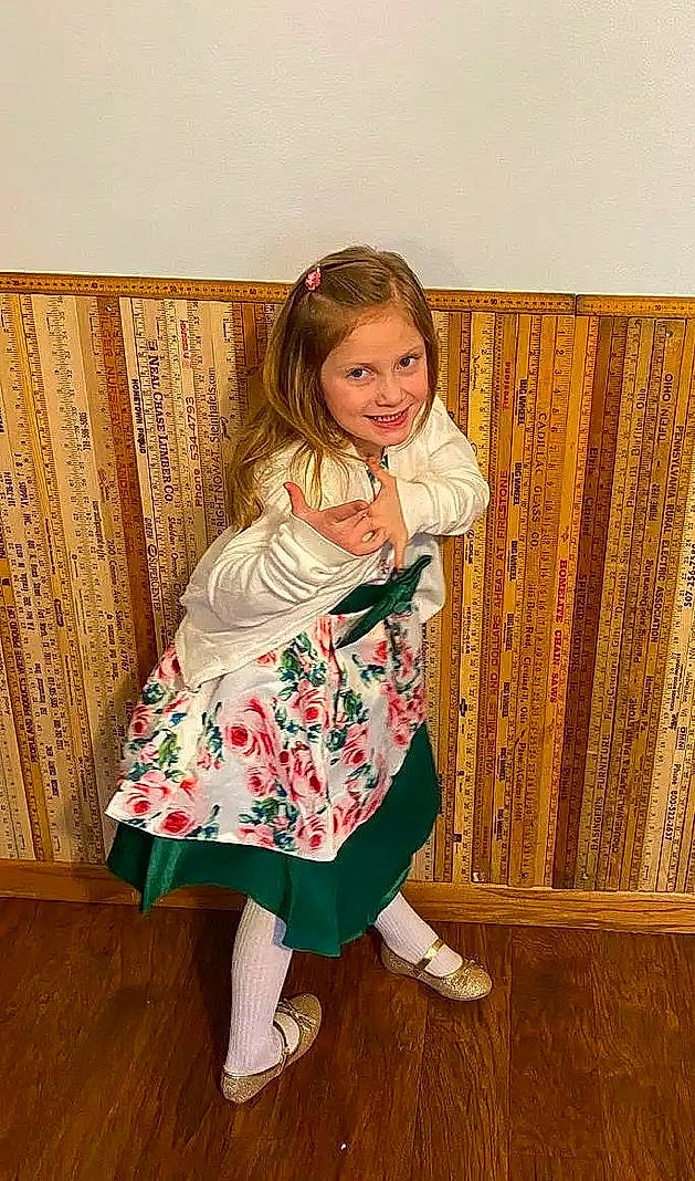 Mara is registered to the contest to win money with this photo: baby_toddler_clothing, dress, facial_expression, floor, flooring, footwear, fun, hair, happy, hardwood, human_body, human_leg, joy, long_hair, pattern, person, sitting, sleeve, smile, sock