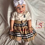 Eleya is registered to the contest to win money with this photo: baby, child, infant, dress, plaid, headband, bow, bracelet, white_blanket, milestone_card, five_months_old, smiling, cute, lying_down, soft_texture, portrait, indoors, person, happy, fashion