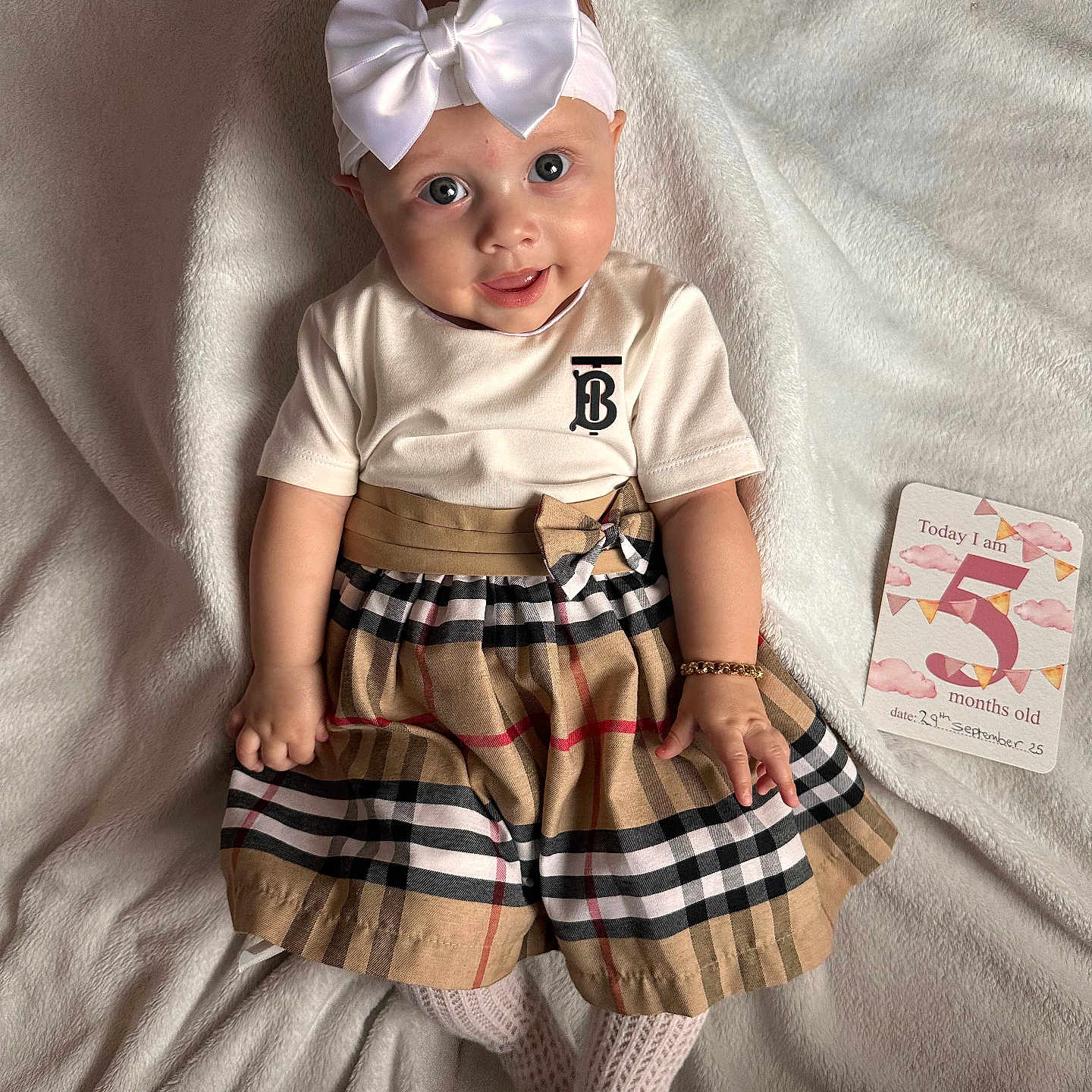 Eleya is registered to the contest to win money with this photo: baby, bow, bracelet, child, cute, dress, fashion, five_months_old, happy, headband, indoors, infant, lying_down, milestone_card, person, plaid, portrait, smiling, soft_texture, white_blanket