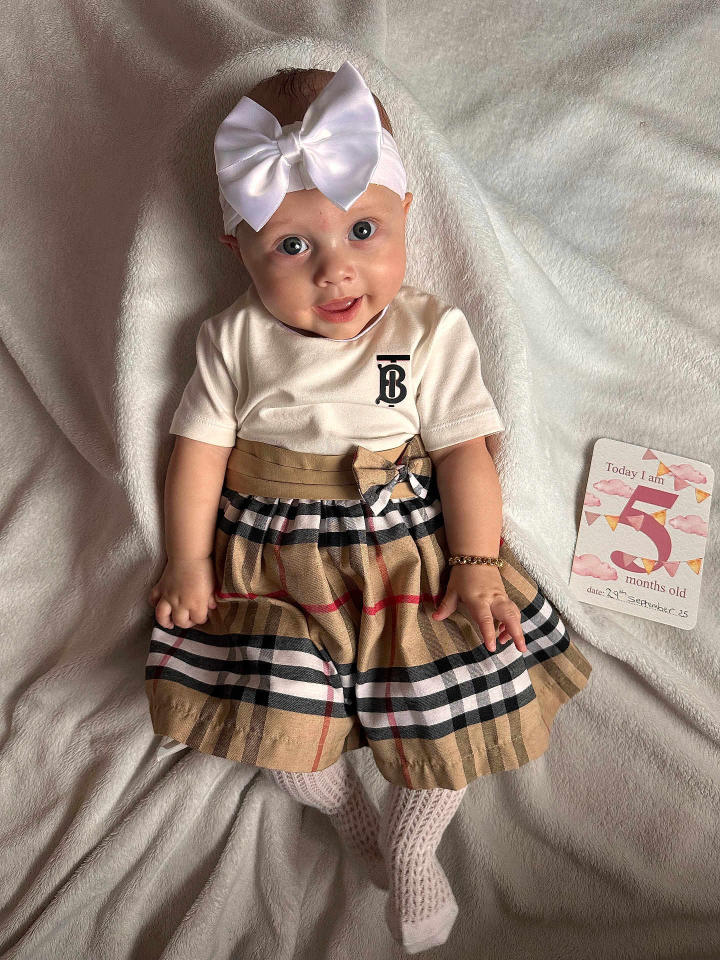 Eleya is registered to the contest to win money with this photo: baby, child, infant, dress, plaid, headband, bow, bracelet, white_blanket, milestone_card, five_months_old, smiling, cute, lying_down, soft_texture, portrait, indoors, person, happy, fashion