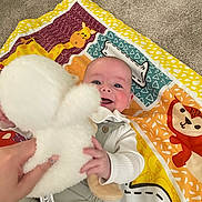 Charlie joined the competition — help win amazing prizes! baby, child, smiling, stuffed_toy, hand, play_mat, colorful, animal_print, indoor, carpet, clothing, person, infant, happy, toy, cute, soft, fabric, portrait, reaching