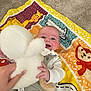 baby, child, smiling, stuffed_toy, hand, play_mat, colorful, animal_print, indoor, carpet, clothing, person, infant, happy, toy, cute, soft, fabric, portrait, reaching