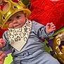 baby, crown, bib, blue_clothing, toy, red_blanket, foam_mat, playroom, infant, child, cute, smiling, indoor, person, headwear, hand, floor, soft_toy, colorful, happy