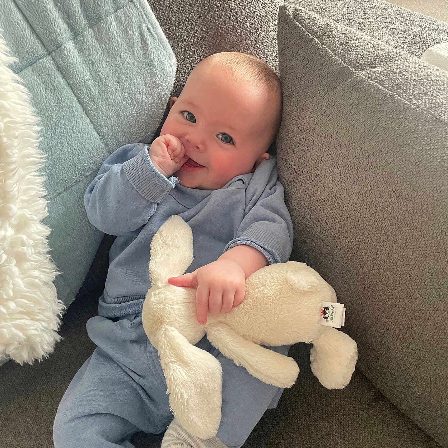 Charlie is registered to the contest to win money with this photo: baby, blanket, blue_pajamas, bunny, carpet, child, couch, cozy, cushion, cute, happy, home, indoor, infant, person, relaxed, smiling, soft_toy, stuffed_animal, thumb_sucking