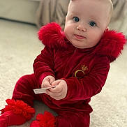 Dolcie-Bleu is registered to the contest to win money with this photo: baby, child, red_clothing, red_bow, sitting, carpet, indoor, soft_texture, cute, portrait, sock, fur_trim, holding_object, face, blue_eyes, infant, cozy, warm_clothing, blanket, couch
