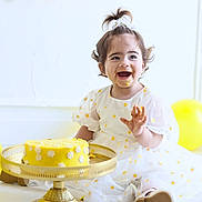 Janna participe au concours pour gagner de l'argent avec cette photo : toddler, child, birthday, cake, yellow, dress, smiling, happy, balloons, celebration, face_paint, flower, party, golden_cake_stand, white_background, floor, sitting, cute, playful, fun