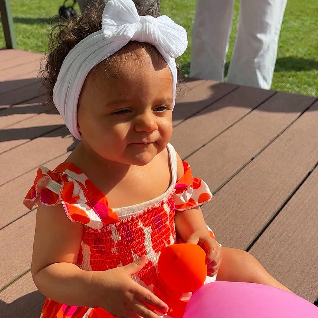 Mayannah participe au concours pour gagner de l'argent avec cette photo : adult, balloon, casual_clothing, child, colorful, dress, family, flower_bush, garden, grass, happy, headband, outdoor, person, play, summer, sunlight, toddler, toy, wooden_deck