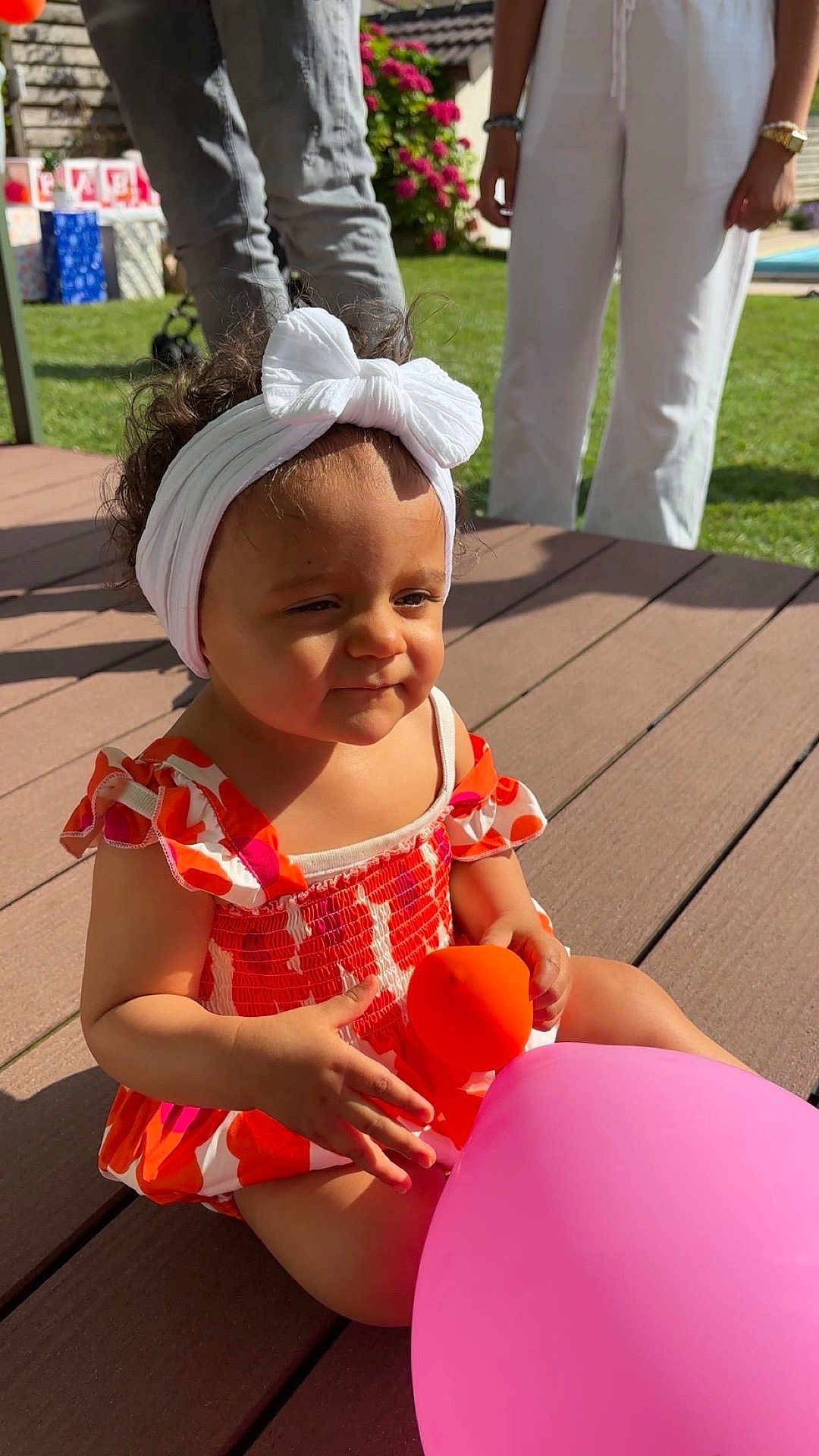 Mayannah participe au concours pour gagner de l'argent avec cette photo : toddler, child, balloon, headband, dress, outdoor, sunlight, garden, grass, adult, wooden_deck, toy, summer, play, happy, colorful, person, flower_bush, casual_clothing, family