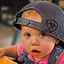 baby, blue_eyes, cap, casual, child, closeup, clothing, curious_expression, denim_overalls, face, hat, headwear, indoor, person, pink_shirt, portrait, seat, table, toddler, young_child