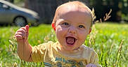 Wylder is registered to the contest to win money with this photo: baby, child, grass, outdoor, smiling, happy, sunlight, nature, greenery, field, toddler, holding, clothing, yellow_shirt, face, expression, person, daylight, playful, cute