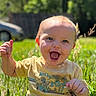 baby, child, grass, outdoor, smiling, happy, sunlight, nature, greenery, field, toddler, holding, clothing, yellow_shirt, face, expression, person, daylight, playful, cute