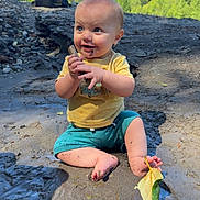 Wylder is registered to the contest to win money with this photo: baby, child, mud, stick, outdoor, nature, trees, sky, grass, dirt, playful, happy, smiling, sitting, yellow_shirt, blue_shorts, barefoot, leaf, sunlight, daytime