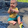 baby, child, mud, stick, outdoor, nature, trees, sky, grass, dirt, playful, happy, smiling, sitting, yellow_shirt, blue_shorts, barefoot, leaf, sunlight, daytime