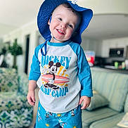 Dayton joined the competition — help win amazing prizes! toddler, child, smile, blue_hat, mickey_mouse, surf_camp, shorts, shirt, indoor, living_room, couch, pillow, happy, portrait, person, clothing, hat, playful, cute, standing