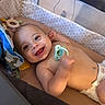Sebastian is registered to the contest to win money with this photo: arm, baby, child, comfort, cushion, cute, diaper, face, hand, happy, head, indoors, infant, lying, pacifier, playpen, resting, skin, smiling, toy