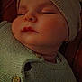 baby, sleeping, knit_sweater, hat, cozy, closeup, infant, face, peaceful, soft_light, warm_colors, button, child, portrait, resting, indoors, cute, skin, headwear, newborn