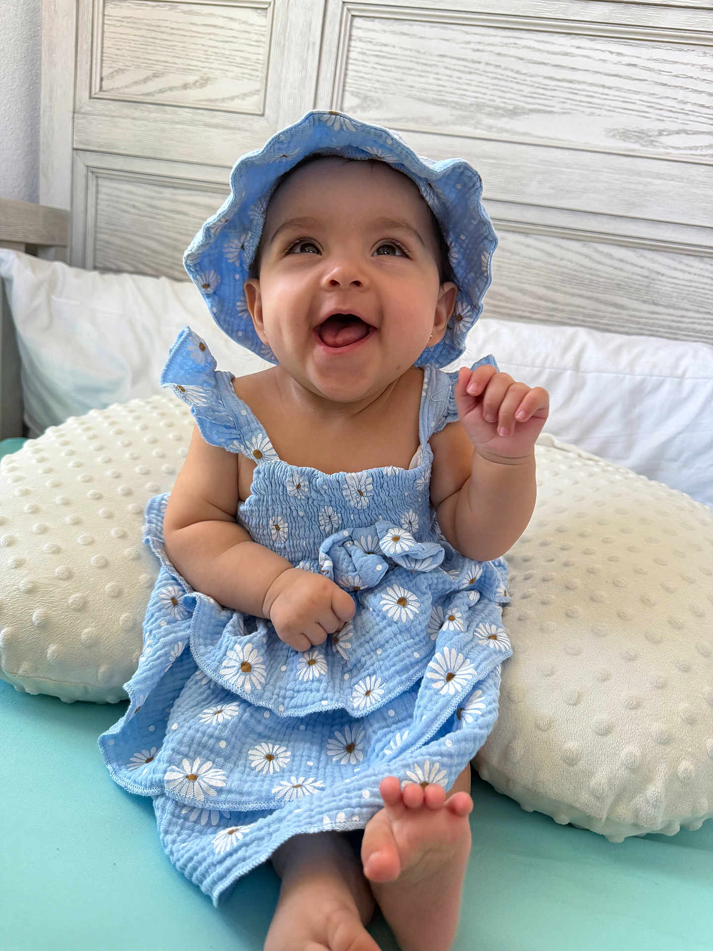 Amanda joined the competition — help win amazing prizes! baby, child, smiling, blue_dress, hat, cushion, indoor, happy, infant, portrait, cute, sitting, foot, hand, skin, clothing, headwear, person, bed, soft_furniture