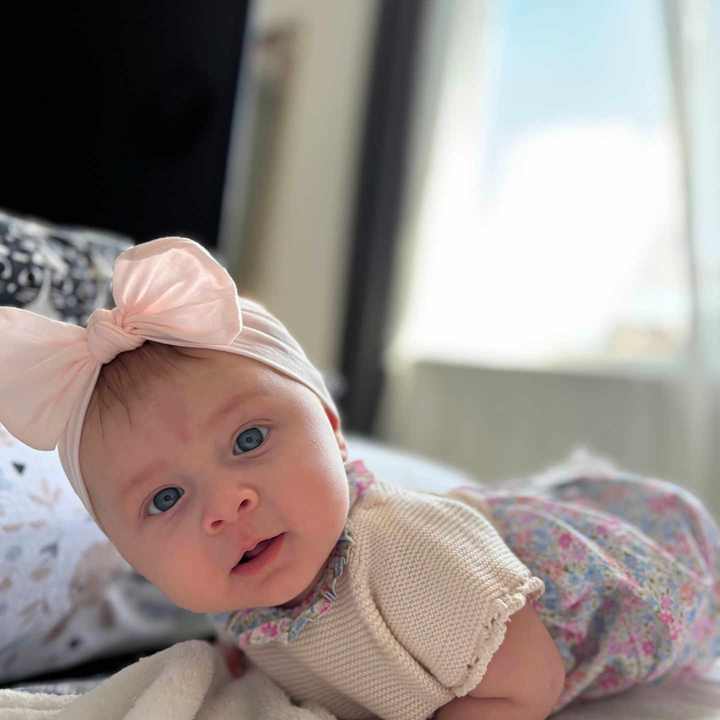 Heïly participe au concours pour gagner de l'argent avec cette photo : baby, blanket, blue_eyes, clothing, curious, cute, expression, face, headband, indoors, infant, knitwear, lying_down, natural_light, person, pink_bow, portrait, soft_texture, toddler, window