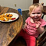 casual, chicken_nuggets, child, dining, dips, flooring, food, french_fries, happy, home, indoor, meal, person, pink_clothing, plate, smiling, toddler, toy, wooden_chair, wooden_table