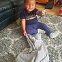 blanket, carpet, child, clothing, curly_hair, expression, floor, furniture, indoor, living_room, pacifier, person, play, plush_toy, rug, sitting, smiling, sofa, toddler, toy