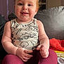 Marvin is registered to the contest to win money with this photo: baby, child, smiling, sitting, red_hair, curly_hair, tank_top, leggings, couch, indoors, face, happy, cute, hands, feet, living_room, furniture, blanket, casual_clothing, portrait