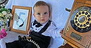 Rafael Mejia joined the competition — help win amazing prizes! baby, child, infant, portrait, sitting, formal_clothing, bow_tie, suspenders, black_pants, white_shirt, socks, antique_telephone, rotary_dial, vintage, outdoor, garden, flowers, blanket, framed_number, furniture