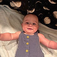 Braxton is registered to the contest to win money with this photo: baby, infant, smiling, romper, blue_clothing, blanket, moon_pattern, lying_down, arms_outstretched, happy, cute, child, face, head, eyes, skin, buttoned_clothing, indoors, soft_texture, comfort