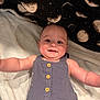 baby, infant, smiling, romper, blue_clothing, blanket, moon_pattern, lying_down, arms_outstretched, happy, cute, child, face, head, eyes, skin, buttoned_clothing, indoors, soft_texture, comfort