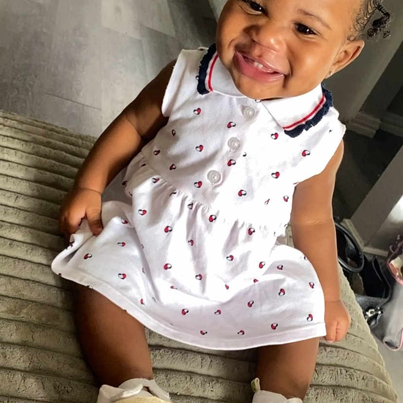 Janorii is registered to the contest to win money with this photo: toddler, child, smiling, white_dress, red_bow, indoor, flooring, happy, sitting, baby_shoes, curly_hair, cute, portrait, person, young_child, home, carpet, candid, playful, fashion