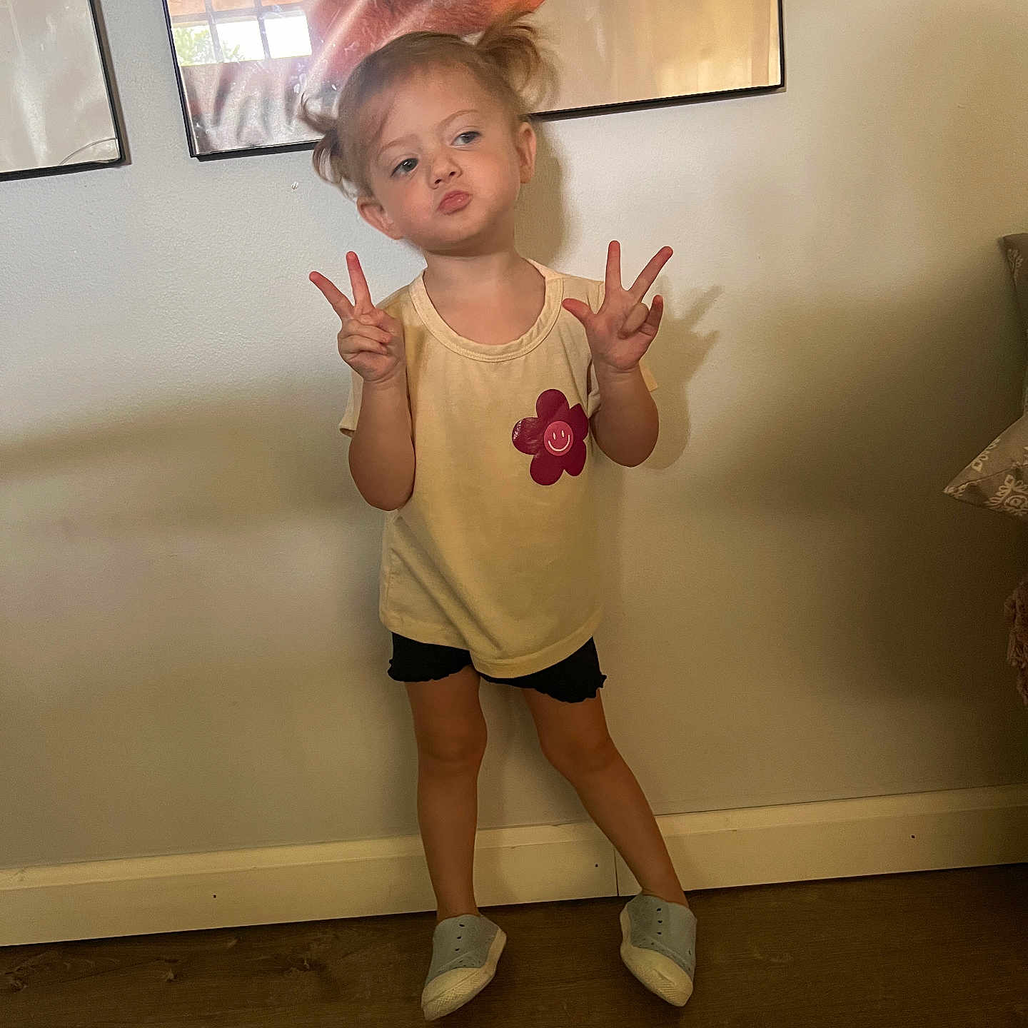 Madelyn joined the competition — help win amazing prizes! black_shorts, casual_clothing, child, cute, expression, framed_picture, girl, indoor, peace_sign, pigtails, playful, posing, puckered_lips, shadow, smiling_flower, standing, wall_art, wooden_floor, yellow_shirt, young