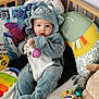 baby, child, dinosaur_onesie, toy, cushion, nursery, plush_toy, colorful, playful, soft_toys, infant, cute, indoor, floor_play, smiling, seated, clothing, face, hand, expression