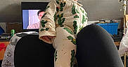 Michael is registered to the contest to win money with this photo: baby, child, onesie, cactus_pattern, legs, blanket, television, indoor, person, furniture, room, face, expression, footed_pajamas, seated, casual, couch, blanket_edge, screen, living_room