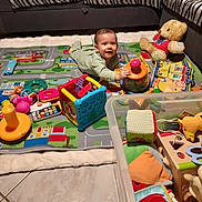 Julio participe au concours pour gagner de l'argent avec cette photo : baby, toddler, toy, play_mat, living_room, couch, teddy_bear, child, floor, colorful, plastic_toys, soft_toys, playtime, smiling, indoors, cushion, puzzle_toy, clothing, person, happy