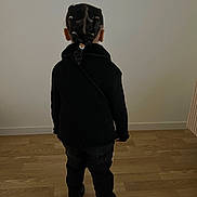 Naïla a rejoint le concours — aidez-le/la à gagner de superbes lots ! child, braided_hair, black_clothing, standing, back_view, indoor, wooden_floor, plain_wall, casual, young, person, hair_ties, flooring, childhood, minimalist, portrait_style, small_person, fashion, hairstyle, home