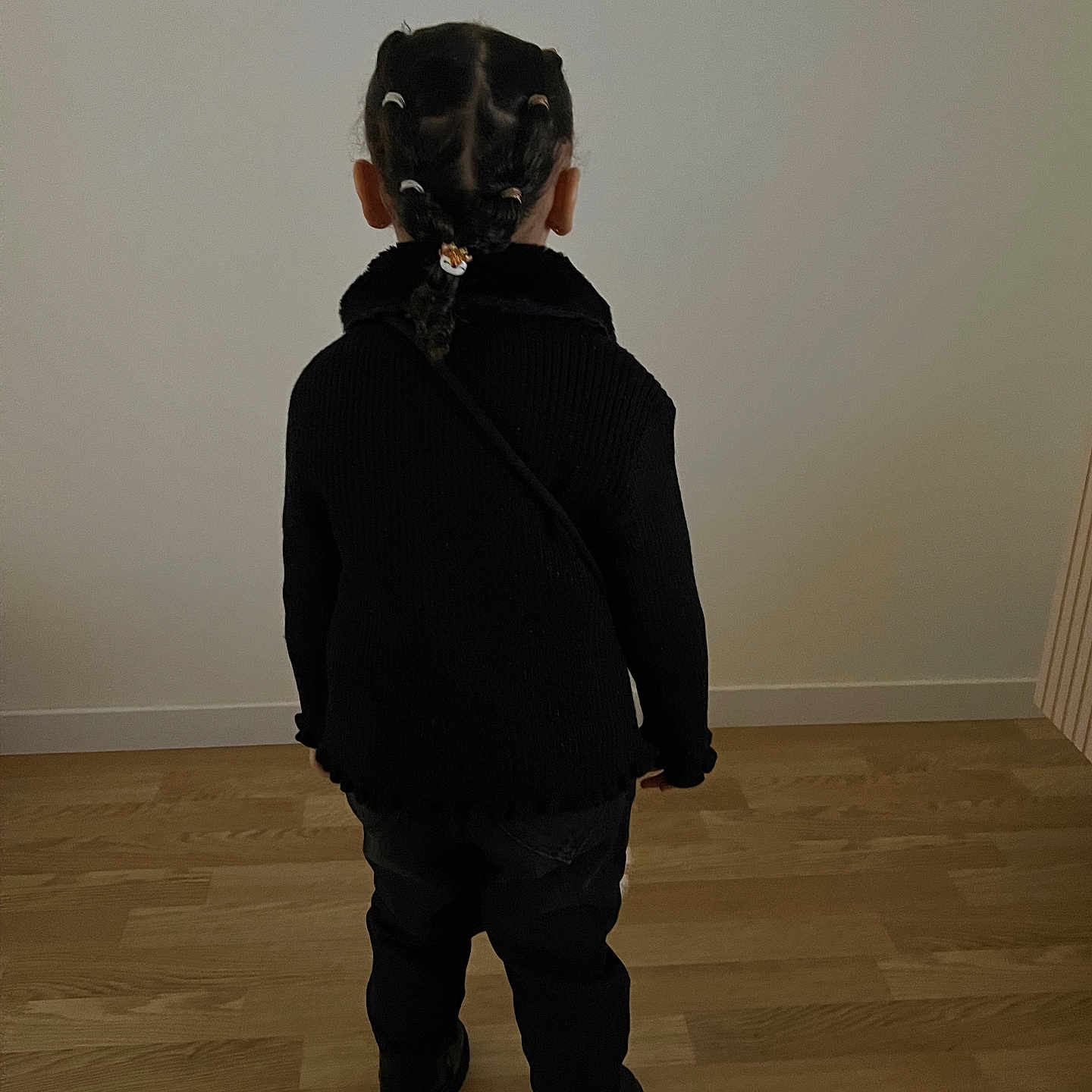 Naïla a rejoint le concours — aidez-le/la à gagner de superbes lots ! back_view, black_clothing, braided_hair, casual, child, childhood, fashion, flooring, hair_ties, hairstyle, home, indoor, minimalist, person, plain_wall, portrait_style, small_person, standing, wooden_floor, young