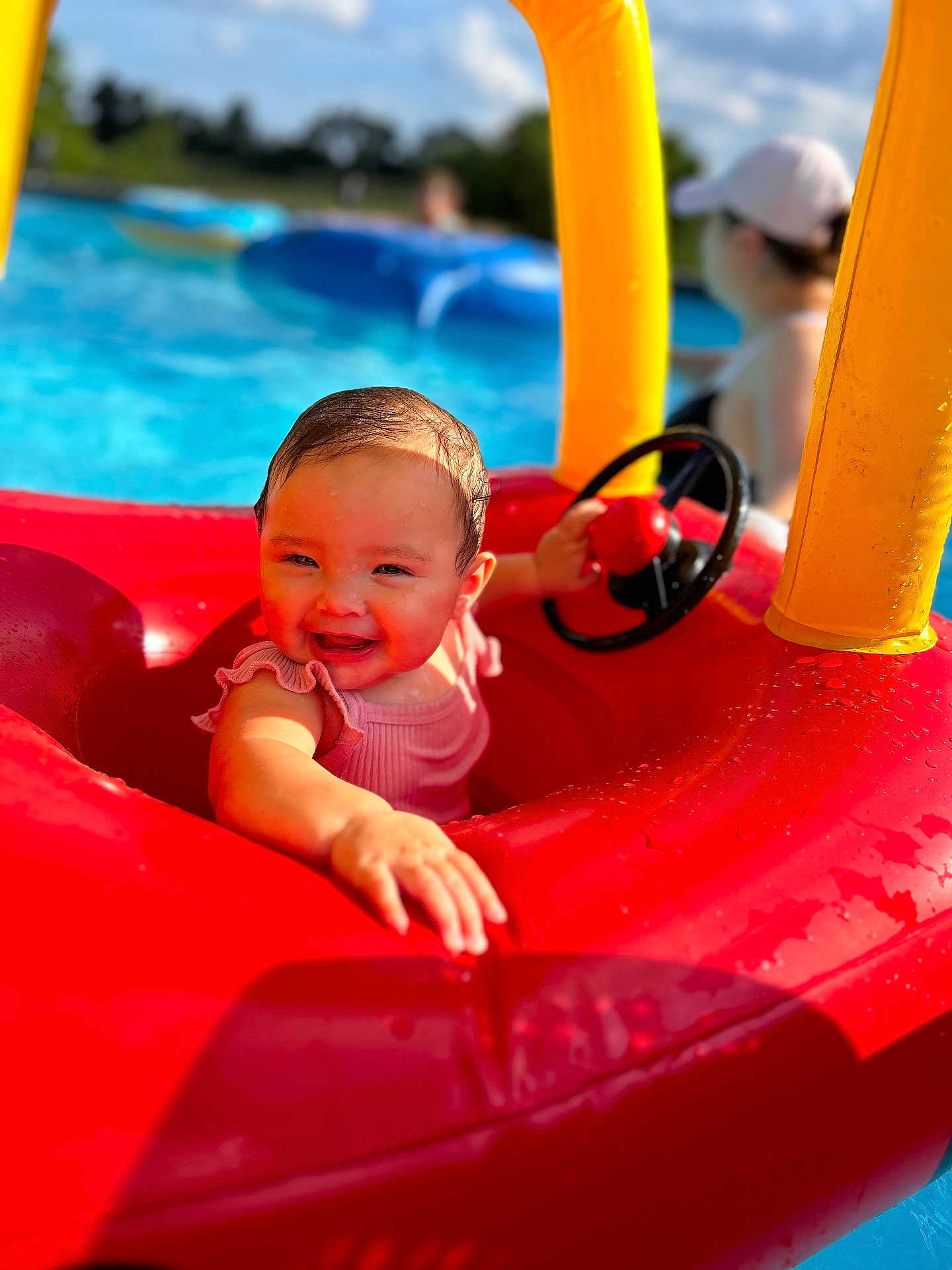 Mia is registered to the contest to win money with this photo: baby, child, pool, inflatable, float, red, yellow, water, summer, outdoor, steering_wheel, smiling, cap, playing, fun, sunlight, happy, person, swimming, toy