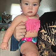 Mia is registered to the contest to win money with this photo: baby, child, indoor, person, swimsuit, pink_clothing, holding, hand, face, expression, furniture, window, light, adult_hand, ring, floor, tile, hairclip, curious, serious