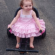 Lilyanna is registered to the contest to win money with this photo: child, clothing, dress, eveningdress, face, female, formalwear, girl, gun, head, machine, person, photography, portrait, road, sitting, tire, transportation, weapon, wheel
