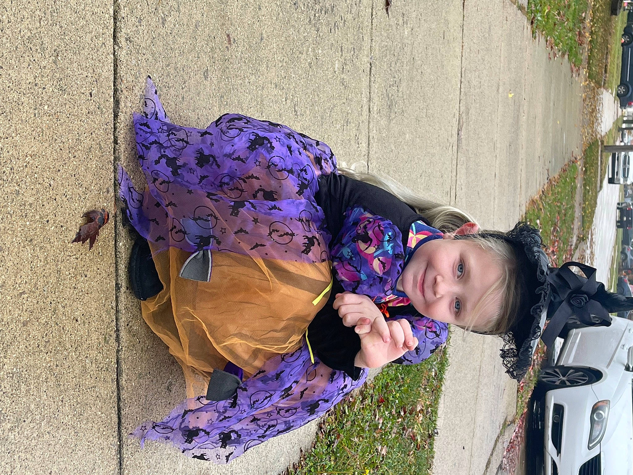 Kinsley is registered to the contest to win money with this photo: car, child, costume, electric_blue, fun, grass, headwear, joy, leisure, magenta, pattern, person, plant, purple, sidewalk, sitting, toddler, tree, violet, winter