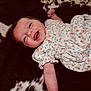 baby, child, smile, happy, dress, floral, infant, lying_down, drool, skin, arm, face, person, cute, small, pattern, black, white, background, joyful