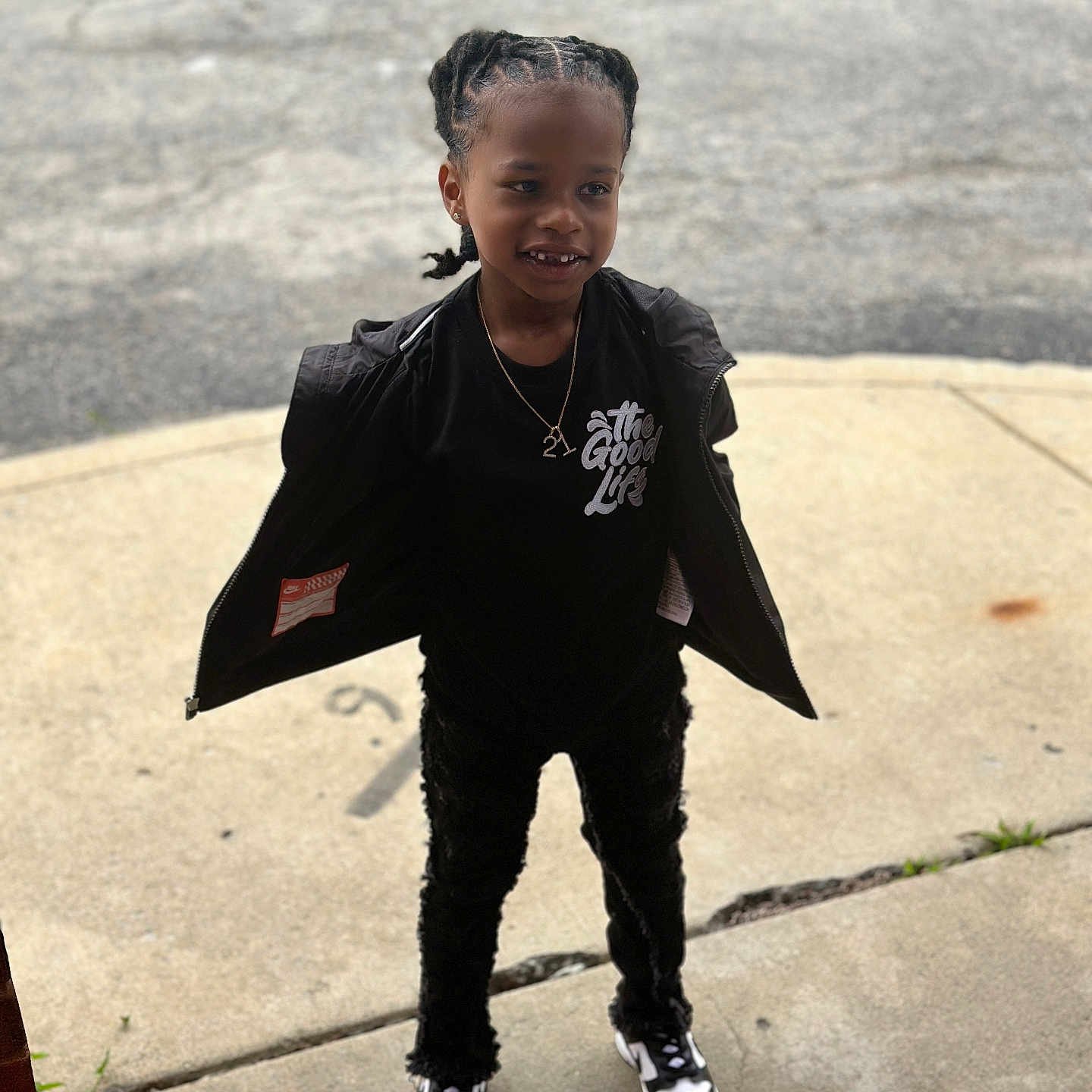 Jaquale is registered to the contest to win money with this photo: black_jacket, black_pants, black_shirt, braided_hair, casual_clothing, child, concrete, daylight, fashion, happy, outdoor, person, portrait, sidewalk, smile, sneakers, standing, street, white_text, young_child