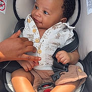 Jamiere is registered to the contest to win money with this photo: baby, child, car_seat, smiling, holding_hand, clothing, buttoned_shirt, shorts, safety_harness, infant, cute, happy, portrait, seated, skin, hand, foot, indoor, person, closeup