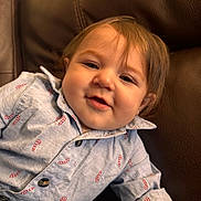 Kolton is registered to the contest to win money with this photo: toddler, child, smiling, shirt, candy_cane_print, blue_shirt, buttoned_shirt, couch, leather_couch, indoor, portrait, happy, cute, face, young_child, casual, relaxed, seated, holiday_theme, baby
